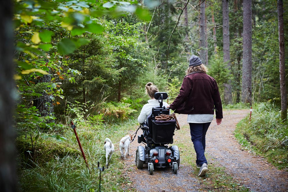 Handikappad tjej med assistent och hund i skogen